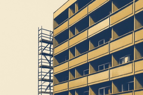 Fassade eines deutschen Mehrfamilienhauses mit Balkonen, ein Balkon mit kleiner Split‑Außeneinheit und Gerüst für Balkonsanierung